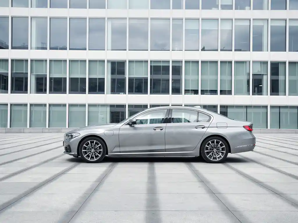 Zilveren zakensedan geparkeerd voor modern glazen kantoorgebouw met geometrische schaduwen op het wegdek