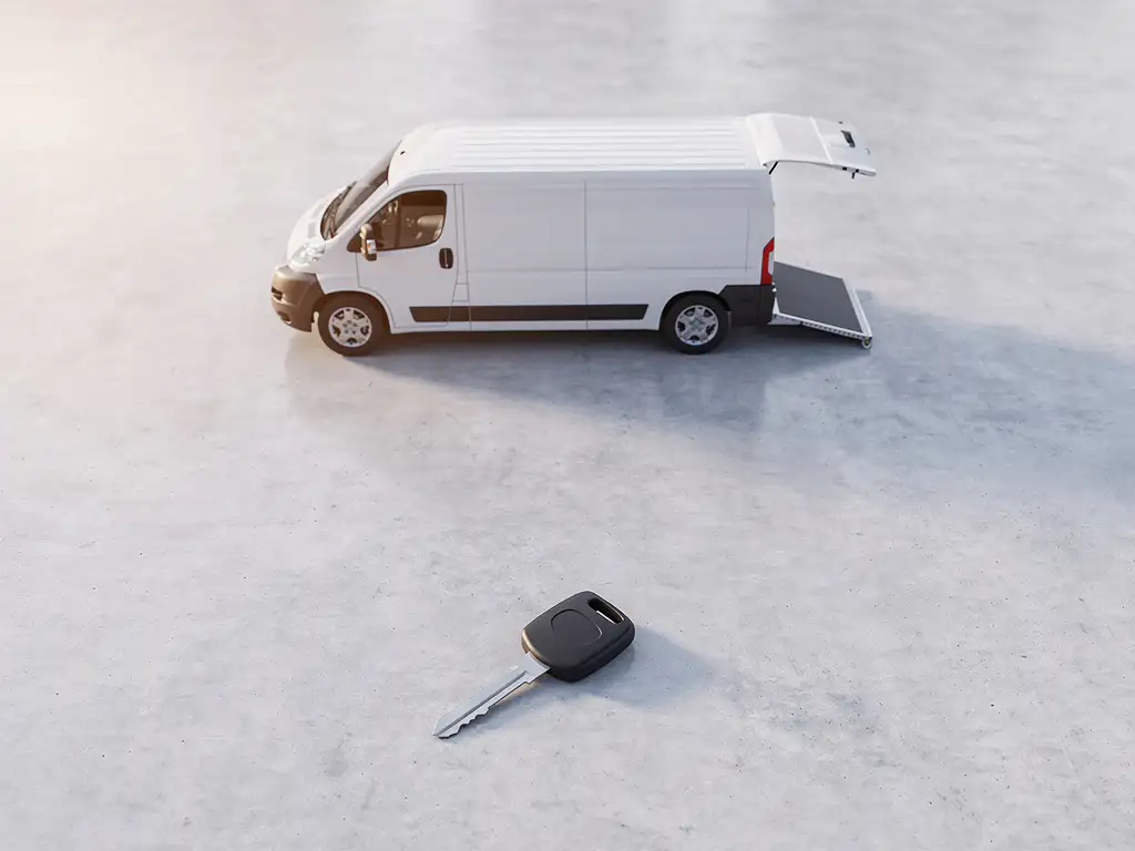 Witte bestelbus met neergeklapte laadklep op betonnen ondergrond, met autosleutel op de voorgrond.