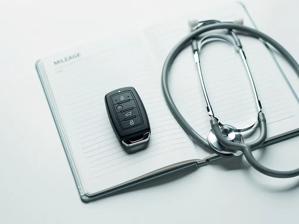 Autosleutel en kilometerregistratieboekje op wit bureau met stethoscoop, voor zorgprofessionals die zakelijke reiskosten bijhouden.