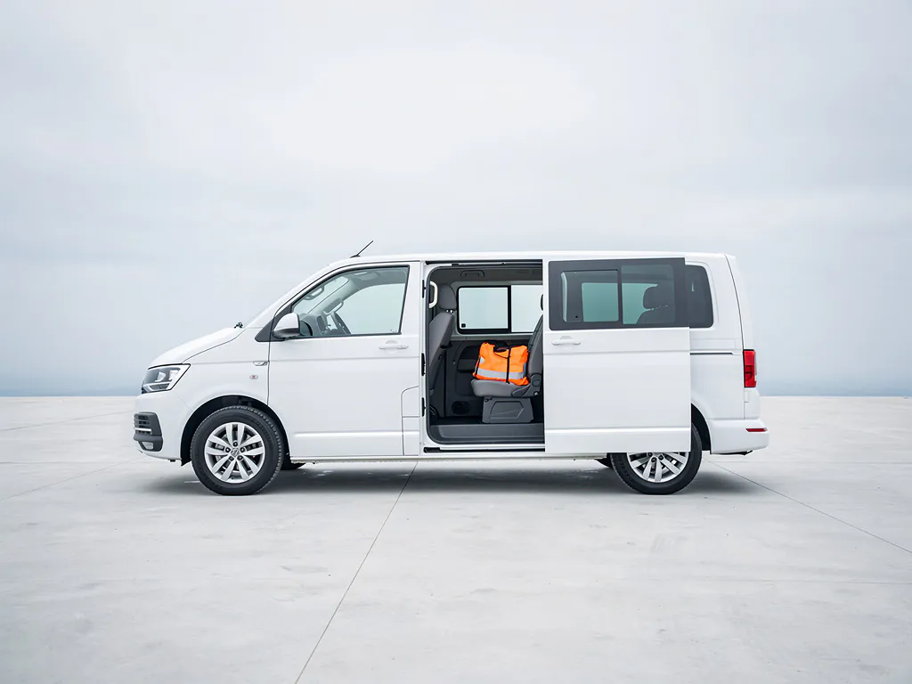 Witte minibus geparkeerd op beton met een oranje veiligheidsvest op de voorstoel, zichtbaar via de open schuifdeur.