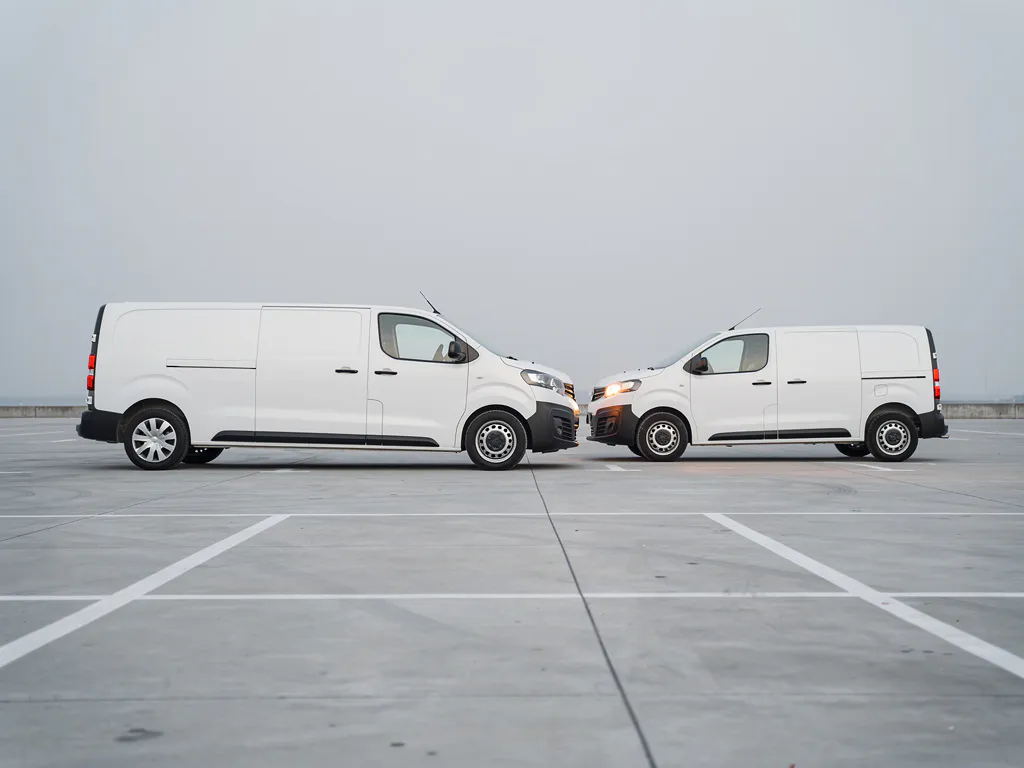 Witte bouwbus en reservebestelwagen geparkeerd op een rustig terrein in zacht ochtendlicht.