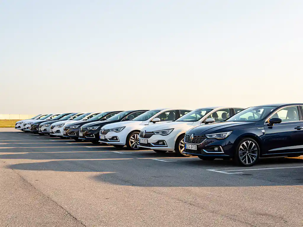 Nette rij huurwagens op een open parkeerterrein in ochtenglicht, één auto iets naar voren getrokken voor directe beschikbaarheid.
