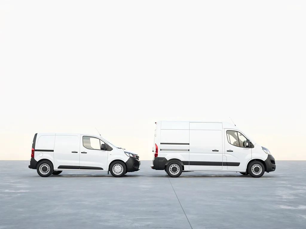 Compacte witte bestelwagen naast een grote witte paneelauto op grijs beton, gefotografeerd op ooghoogte in zacht daglicht.