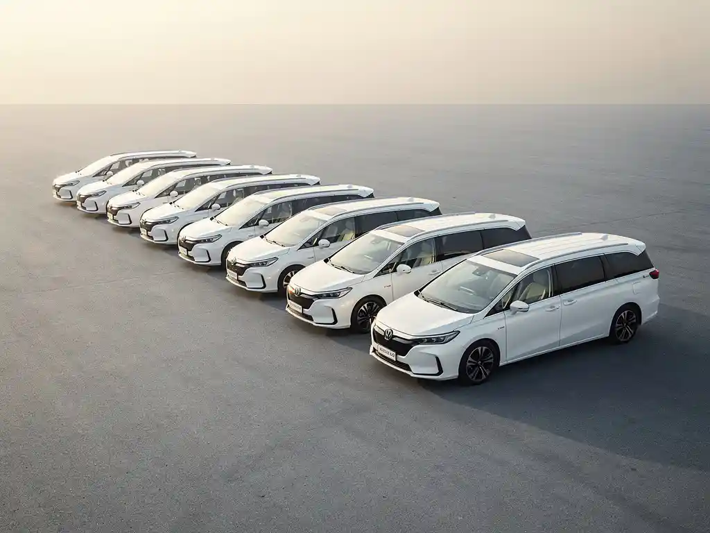 Rij identieke witte minibussen geparkeerd op een grijze parkeerplaats, één busje iets naar voren getrokken, vroeg ochtendlicht.