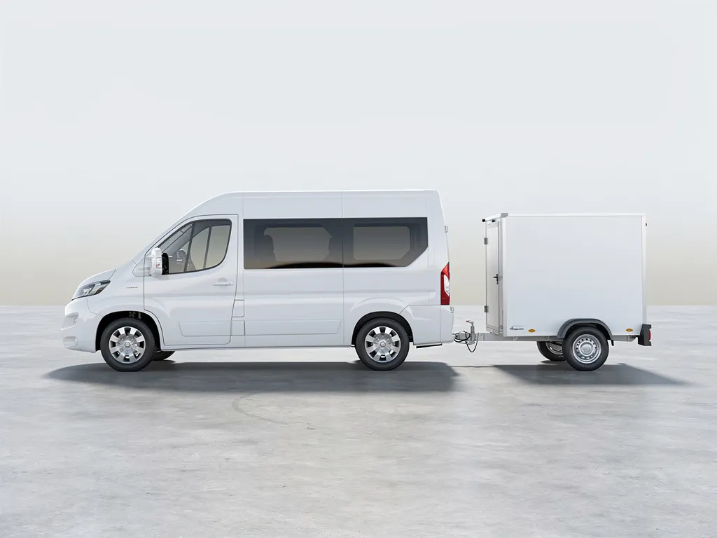 Witte bestelbus met aanhanger geparkeerd op een vlakke ondergrond in zacht daglicht, zijaanzicht.
